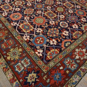 Navy and red geometric rug with intricate floral motifs and colorful accents on rustic wood plank flooring.