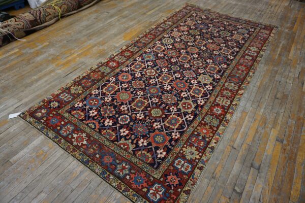 Rectangular dark blue rug with colorful geometric pattern laid on a worn wooden floor.