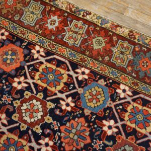Detailed navy rug with red and gold geometric medallions rests diagonally on distressed wood planks.
