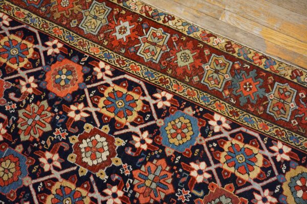 Detailed navy rug with red and gold geometric medallions rests diagonally on distressed wood planks.