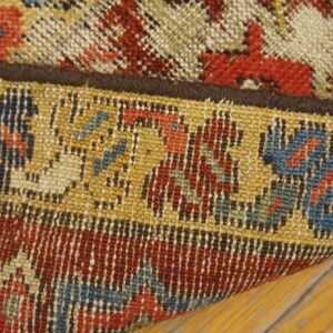 Close-up of a low-pile rug edge folded over distressed wood, featuring geometric red, blue, and yellow patterns.