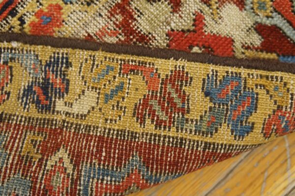 Close-up of a low-pile rug edge folded over distressed wood, featuring geometric red, blue, and yellow patterns.