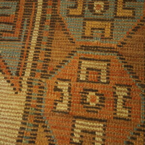 Geometric flatweave rug texture in rust, brown, and teal, resting beside a light wood floor.