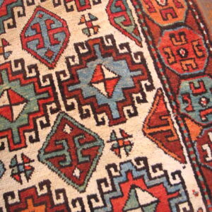 A close-up shows complex geometric patterns in cream, red, blue, and green on hardwood flooring.