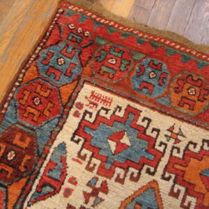 Geometric rug corner featuring red, blue, and ivory tribal designs resting on plank wood flooring.