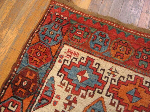 Geometric rug corner featuring red, blue, and ivory tribal designs resting on plank wood flooring.