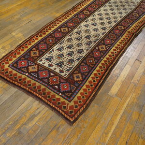 Geometric runner rug in rust, brown, gold, and tan on a distressed, patchy wood plank floor.