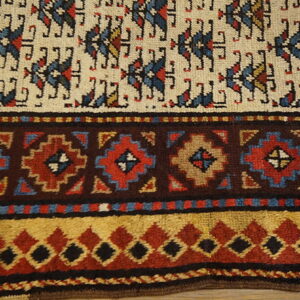 Textured rug detail showing cream field motifs and stepped borders in dark brown, red, blue, and gold.