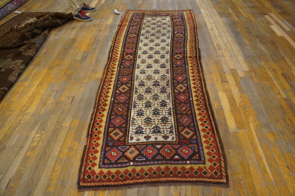 Multicolored geometric runner rug displays tribal patterns on wood floor next to legs in sneakers.