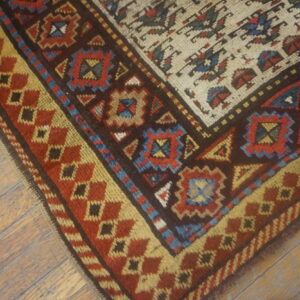Geometric rug corner featuring red, brown, gold, and blue patterns rests on distressed plank flooring.