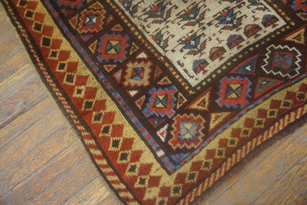Geometric rug corner featuring red, brown, gold, and blue patterns rests on distressed plank flooring.