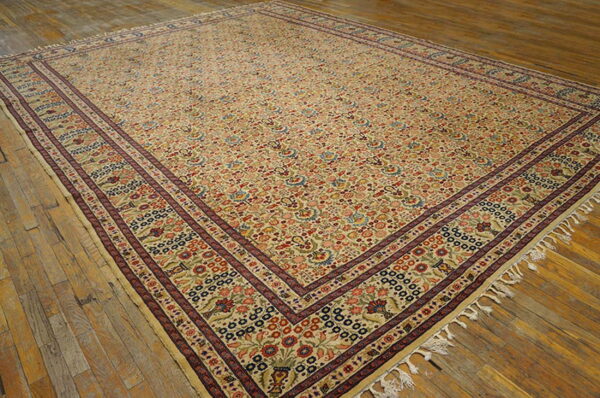 Beige rug with all-over multicolored floral patterns and wide dark red borders on wood flooring.