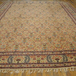 Low-pile beige rug with a busy multicolored floral pattern and complex dark borders on a wood floor.