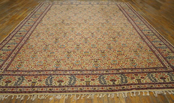 Low-pile beige rug with a busy multicolored floral pattern and complex dark borders on a wood floor.