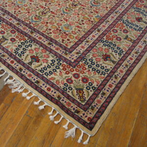 A corner of a cream rug with red and blue floral patterns and tassels on plank wood flooring.
