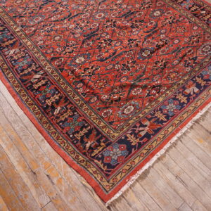 Detailed red rug with blue, gold, and green patterns rests on distressed gray and orange wooden floor.