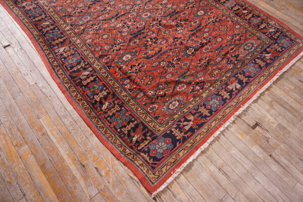 Detailed red rug with blue, gold, and green patterns rests on distressed gray and orange wooden floor.