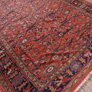 Low-pile red rug with intricate navy and blue floral patterns rests on weathered wooden planks.