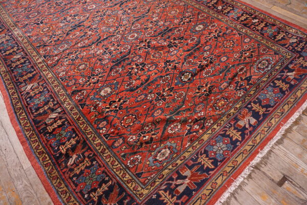 Low-pile red rug with intricate navy and blue floral patterns rests on weathered wooden planks.