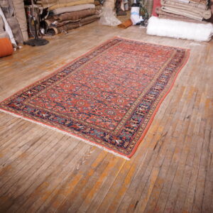 Low-pile orange and blue patterned runner rug displayed on wide, distressed wood plank flooring.