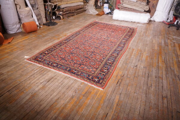 Low-pile orange and blue patterned runner rug displayed on wide, distressed wood plank flooring.