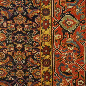 Detailed view of a navy, red, and gold patterned rug border resting on light, distressed wood plank flooring.