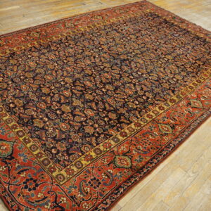 Dark blue patterned rug with red and gold borders lies on light, worn hardwood flooring.