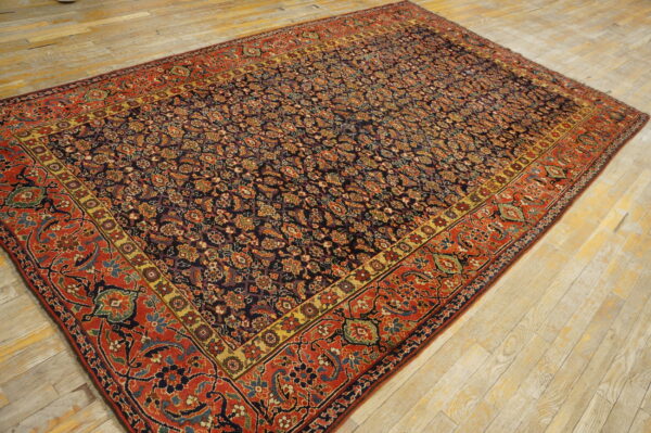 Dark blue patterned rug with red and gold borders lies on light, worn hardwood flooring.