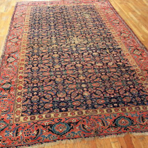 Large area rug featuring a dense floral pattern with navy, coral, and tan colors on a plank hardwood floor.