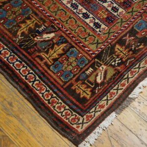 A dark geometric rug with red, blue, and gold patterns rests on distressed golden wood planks.