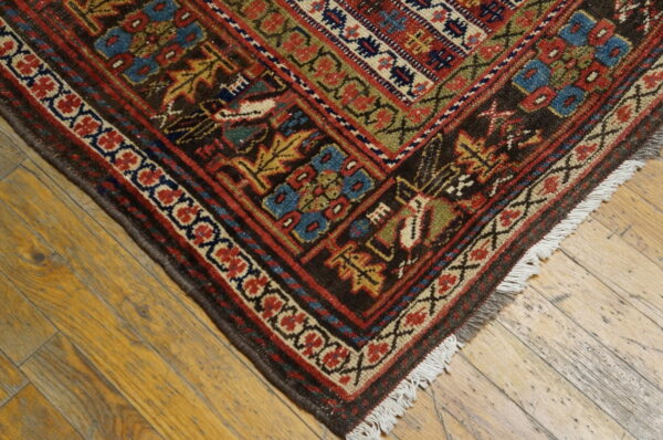 A dark geometric rug with red, blue, and gold patterns rests on distressed golden wood planks.