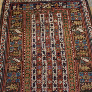 Geometric rug with a vertically striped center and tribal motifs in red, navy, and brown on distressed wood floorboards.