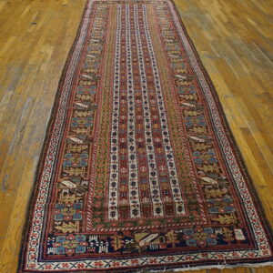 Red, blue, and brown low-pile runner rug with complex tribal patterns on plank hardwood flooring.