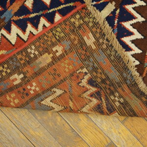A colorful tribal rug is folded back, showing the geometric pattern, fringe, and backing on wood floorboards.