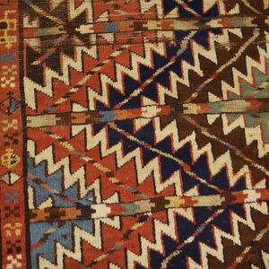 Geometric rug detail showing zigzag patterns in rust, navy, cream, and brown next to wooden flooring.