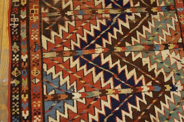 Geometric rug detail showing zigzag patterns in rust, navy, cream, and brown next to wooden flooring.