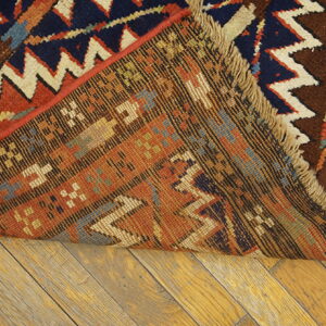 A geometric rug in rust, navy, and cream is folded, revealing the woven reverse on wood plank flooring.
