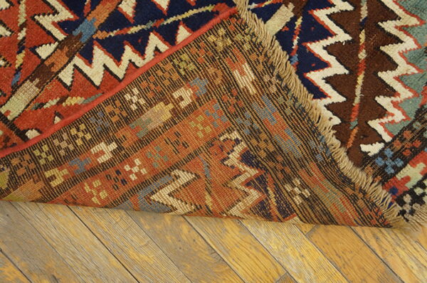 A geometric rug in rust, navy, and cream is folded, revealing the woven reverse on wood plank flooring.