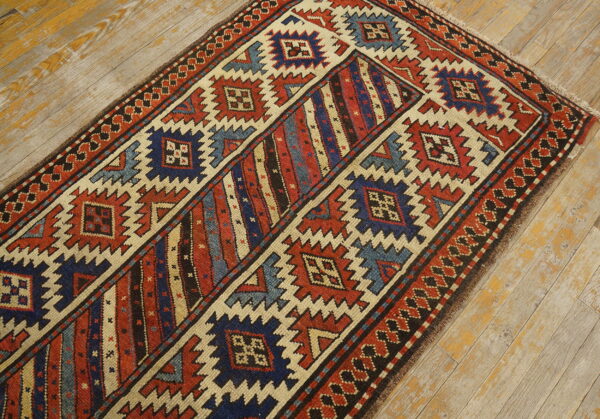 Geometric runner rug featuring red, blue, and cream zigzag designs on distressed light wood plank flooring.