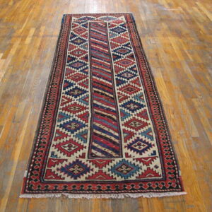 Runner rug with red, navy, cream, and blue geometric patterns lies on a distressed wood floor.