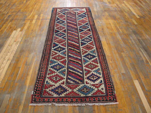 Runner rug with red, navy, cream, and blue geometric patterns lies on a distressed wood floor.