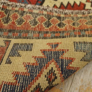 Tightly woven flatweave rug detail in tan, red, and blue geometric patterns over distressed wood.