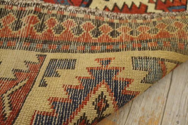 Tightly woven flatweave rug detail in tan, red, and blue geometric patterns over distressed wood.
