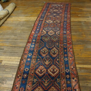 Blue, red, and beige geometric runner rug displayed on a worn wooden floor near bundled textiles.