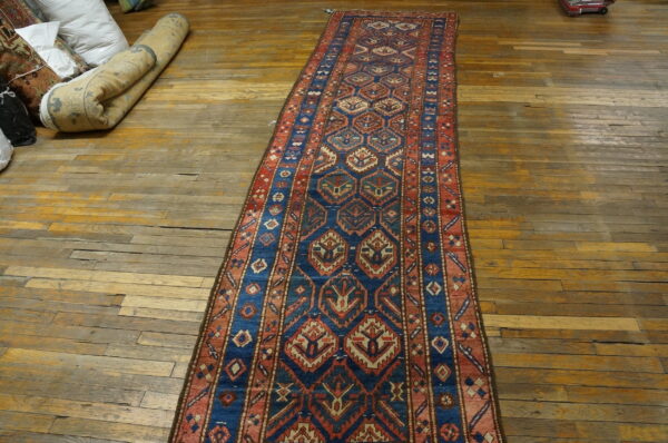 Blue, red, and beige geometric runner rug displayed on a worn wooden floor near bundled textiles.