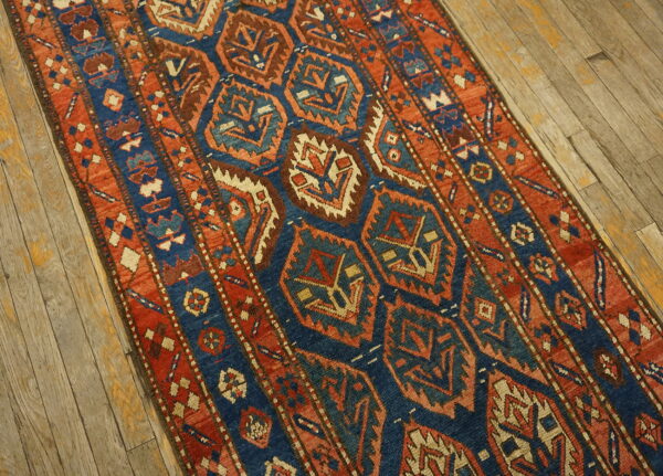 Geometric runner rug in navy blue, rust, and beige on rustic wood plank flooring.