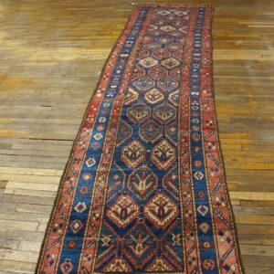 Long runner rug featuring blue and red repeating geometric medallions on aged wood flooring.