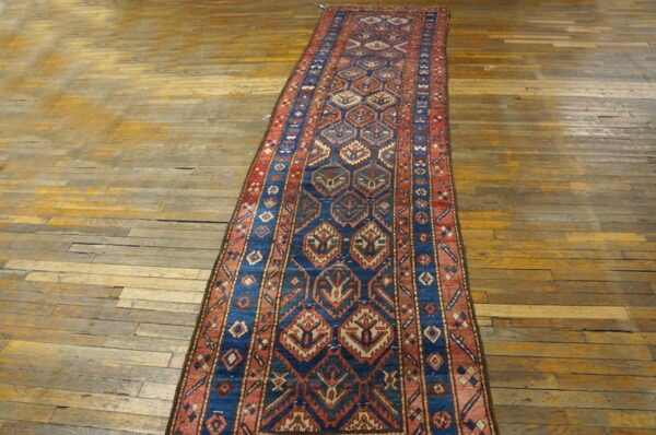 Long runner rug featuring blue and red repeating geometric medallions on aged wood flooring.