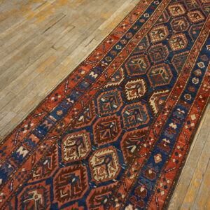Rust red and navy blue geometric runner with repeating medallions lies on weathered wood floorboards.
