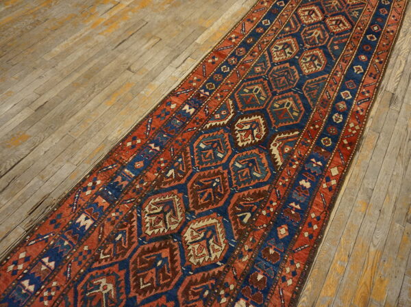 Rust red and navy blue geometric runner with repeating medallions lies on weathered wood floorboards.